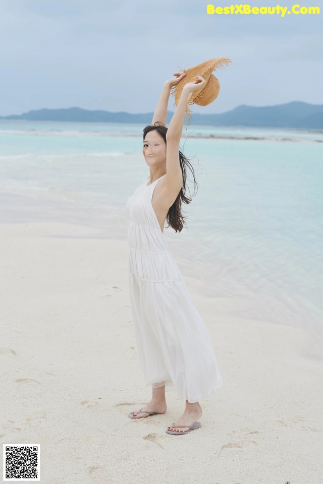 A woman in a white dress and straw hat on the beach.