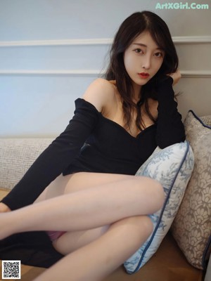 A woman sitting on a couch in a black dress.
