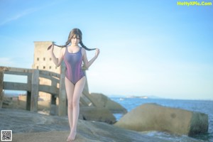 A woman in a bathing suit sitting on a rock by the ocean.