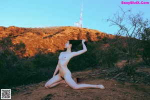 A naked woman standing on a pier next to a yellow lighthouse.