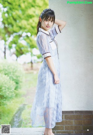 A woman in a blue dress leaning against a wall.