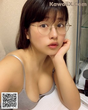 A woman wearing glasses and a black bra sitting on a bed.