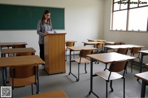 a woman sitting at a desk in front of a blackboard