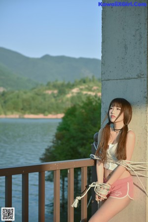 A young woman leaning against a wall with her hands on her hips.