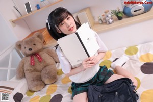 A young woman sitting on a bed holding a book.