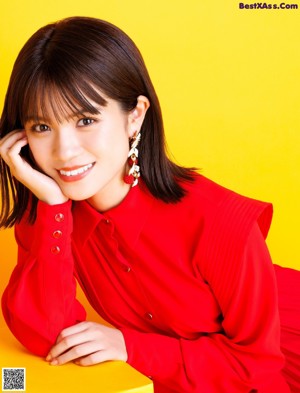 A woman in a red dress sitting on a yellow background.