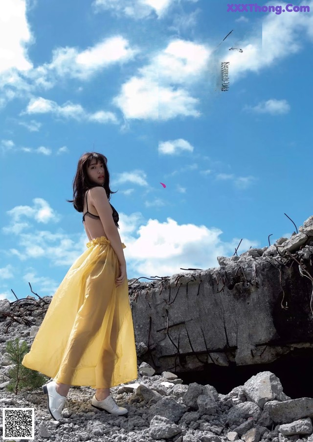 A woman in a yellow dress standing on a rocky hillside.